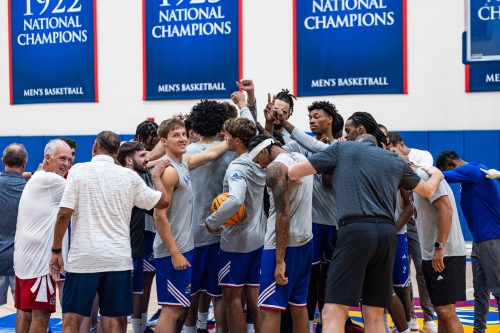 A basketball team gathers in a huddle on the court, surrounded by banners celebrating national championships.